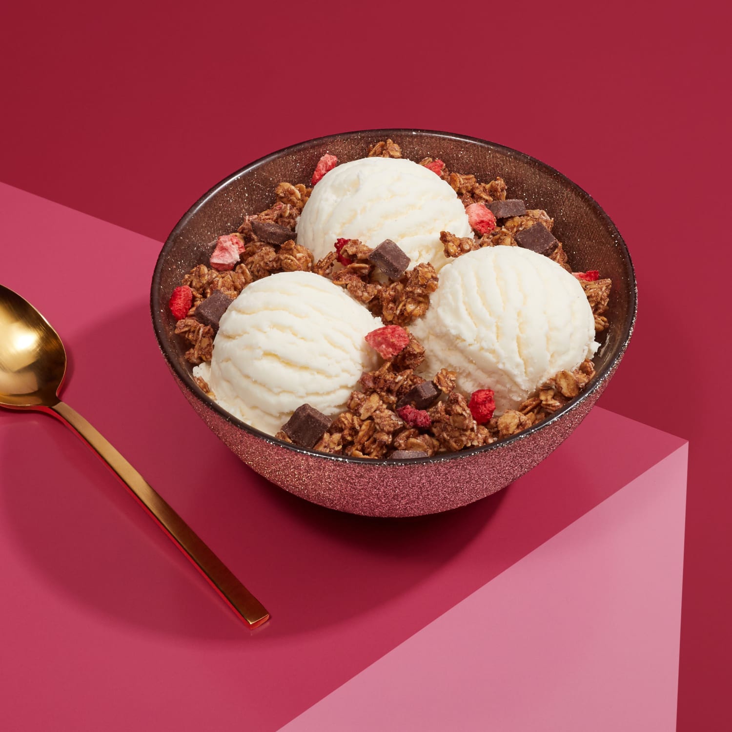 A bowl of three ice cream scoops topped with Love Crunch granola, placed on a table, with a spoon to the side.